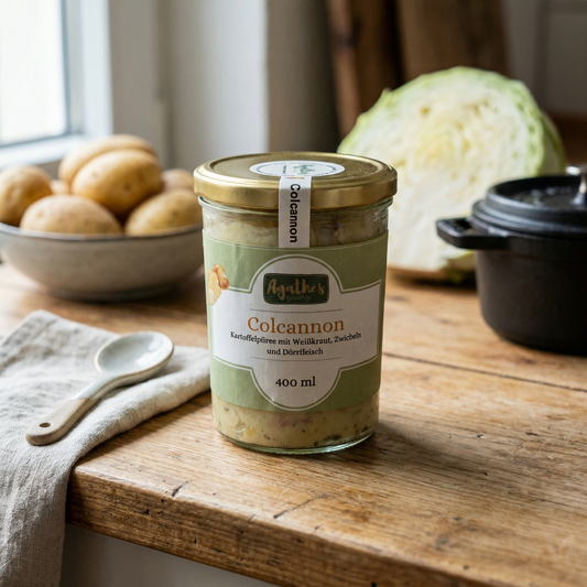 Colcannon im Glas auf einer holzernen Arbeitsfläche, Kartoffeln im Hintergrund

