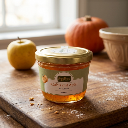 Glas Kürbis-Apfel Brotaufstrich auf einer holzernen Küchenfläche, im Hintergrund dezent ein Apfel und ein Kürbis, Krümel und Puderzucker liegen auch auf dem Tisch